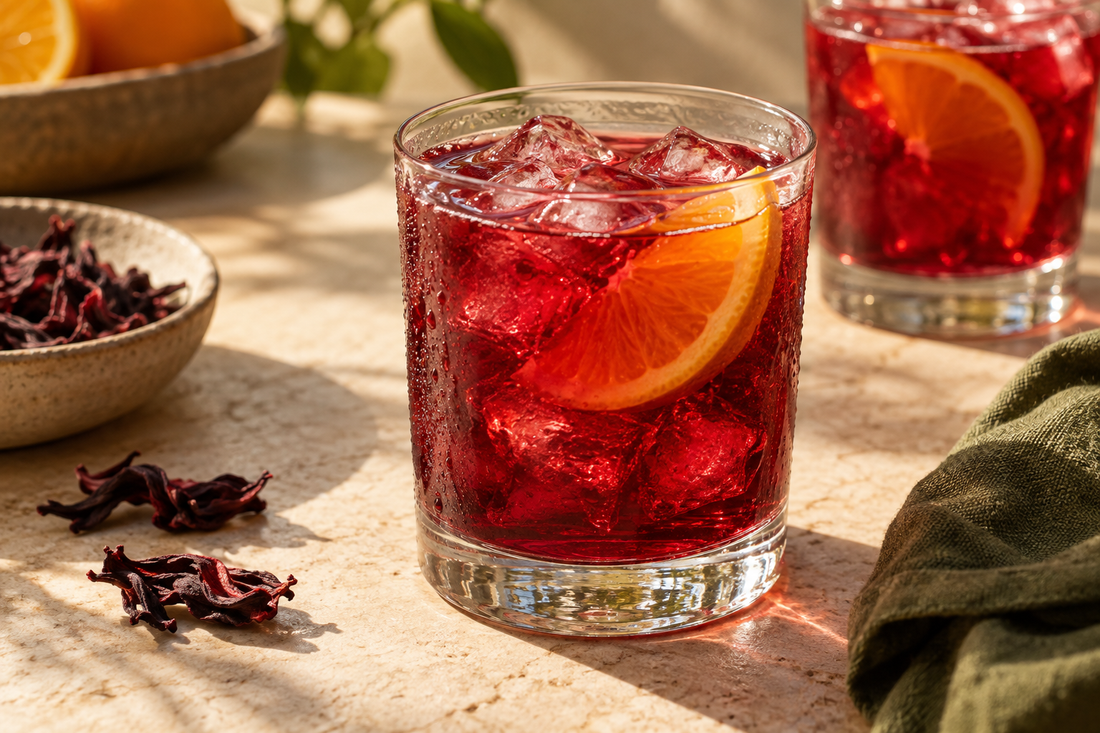 Ruby hibiscus citrus cooler over ice with a thin orange slice in a clear glass; illustrative serving idea.